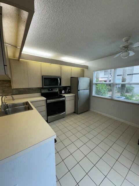 kitchen with ceiling fan, sink, a textured ceiling, light tile patterned flooring, and appliances with stainless steel finishes