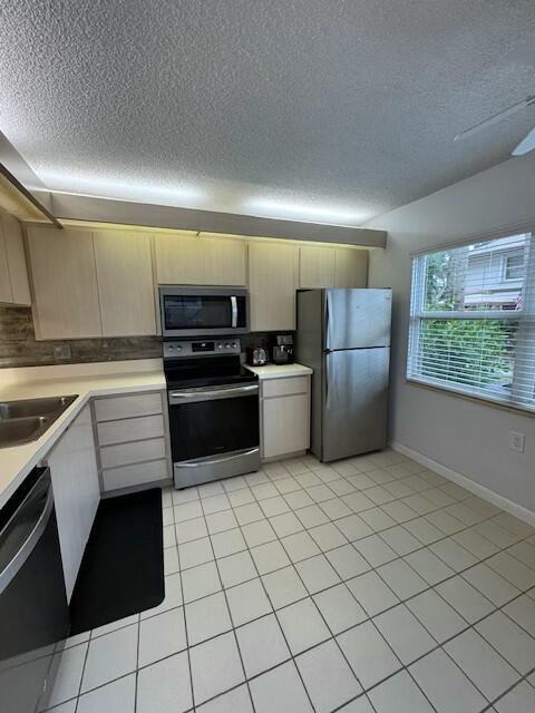 kitchen with light tile patterned floors, sink, appliances with stainless steel finishes, a textured ceiling, and decorative backsplash