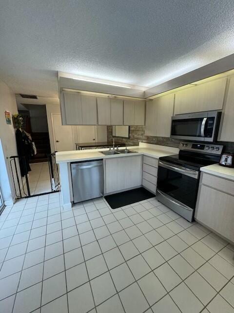 kitchen with stainless steel appliances, sink, a textured ceiling, and light tile patterned floors