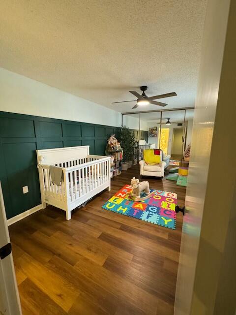 bedroom featuring ceiling fan, dark hardwood / wood-style floors, a textured ceiling, a crib, and a closet