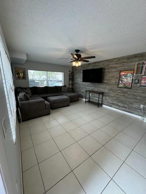 tiled living room featuring ceiling fan, a textured ceiling, and wooden walls