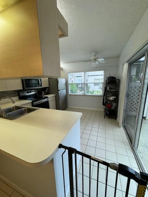 kitchen with sink, light tile patterned floors, a textured ceiling, kitchen peninsula, and stainless steel appliances