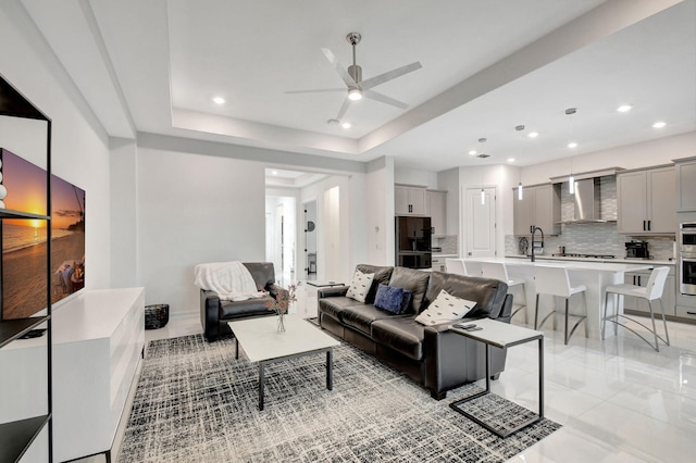 living room featuring sink, ceiling fan, and a tray ceiling