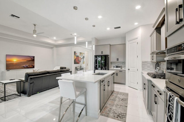 kitchen with an island with sink, decorative backsplash, gray cabinets, ceiling fan, and sink