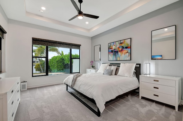 bedroom with a raised ceiling, ceiling fan, and light carpet