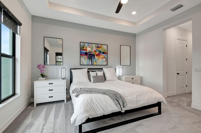 carpeted bedroom featuring multiple windows, ceiling fan, and a tray ceiling