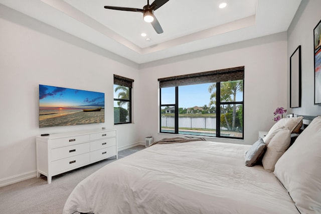 bedroom featuring light carpet, ceiling fan, and a tray ceiling