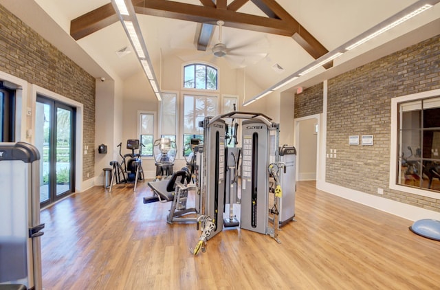 gym with light wood-type flooring, brick wall, ceiling fan, french doors, and high vaulted ceiling