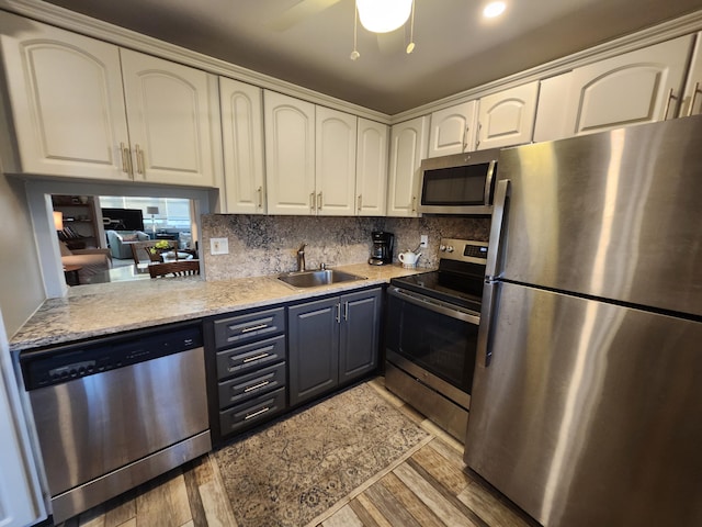 kitchen featuring appliances with stainless steel finishes, decorative backsplash, sink, ceiling fan, and light hardwood / wood-style flooring