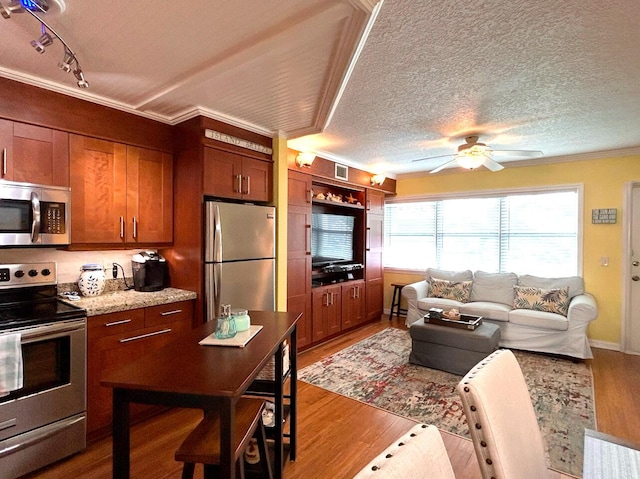 kitchen with stainless steel appliances, ornamental molding, ceiling fan, light stone counters, and a textured ceiling