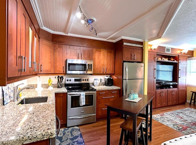 kitchen with stainless steel appliances, sink, light hardwood / wood-style flooring, and light stone countertops