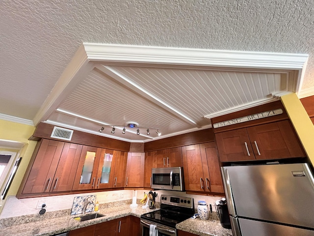 kitchen featuring stainless steel appliances, track lighting, crown molding, light stone counters, and sink