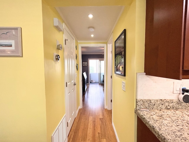 corridor with ornamental molding and light hardwood / wood-style floors