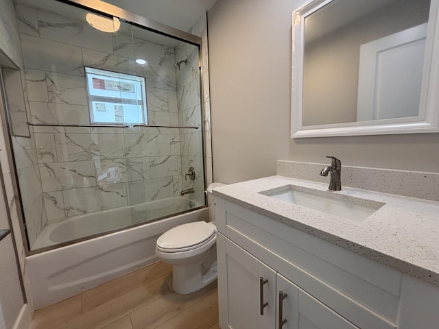 full bathroom with vanity, wood-type flooring, shower / bath combination with glass door, and toilet