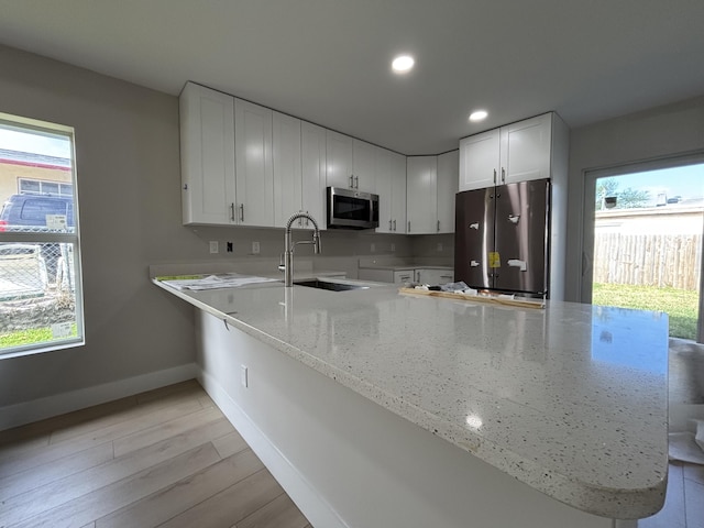 kitchen featuring kitchen peninsula, stainless steel appliances, light hardwood / wood-style floors, white cabinetry, and sink