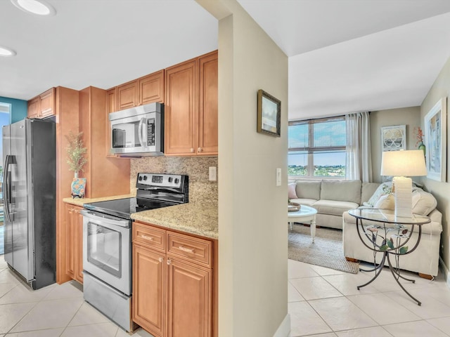 kitchen featuring backsplash, light stone countertops, light tile patterned floors, and appliances with stainless steel finishes