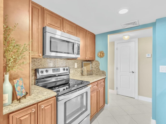 kitchen featuring light tile patterned flooring, light stone counters, backsplash, and appliances with stainless steel finishes