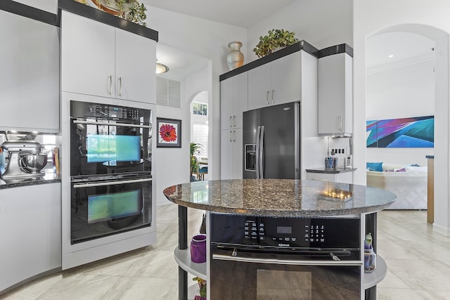 kitchen featuring double oven, light tile patterned floors, fridge with ice dispenser, dark stone countertops, and white cabinets