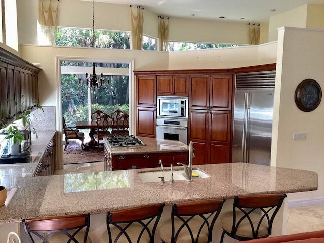 kitchen with sink, a kitchen breakfast bar, built in appliances, a chandelier, and a kitchen island