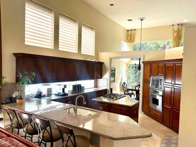 kitchen with a towering ceiling, stainless steel appliances, a kitchen island with sink, sink, and pendant lighting