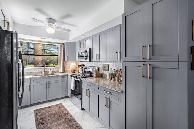 kitchen featuring sink, stainless steel appliances, light stone counters, gray cabinets, and decorative backsplash