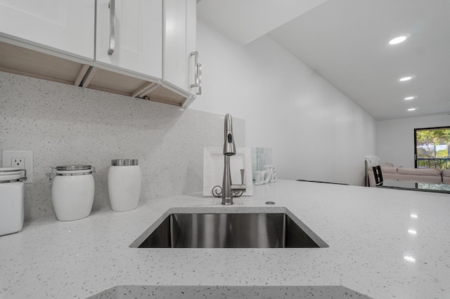 kitchen with white cabinetry, sink, light stone counters, and decorative backsplash