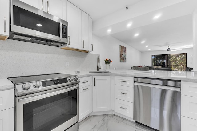 kitchen with appliances with stainless steel finishes, white cabinetry, sink, backsplash, and light stone countertops