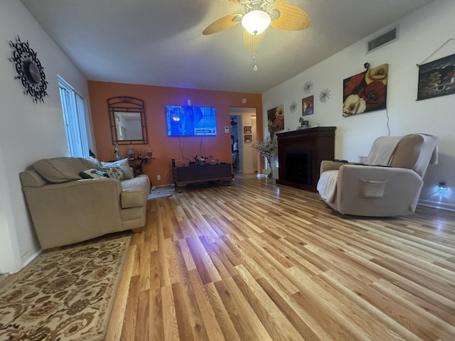 living room with ceiling fan, a textured ceiling, and light wood-type flooring