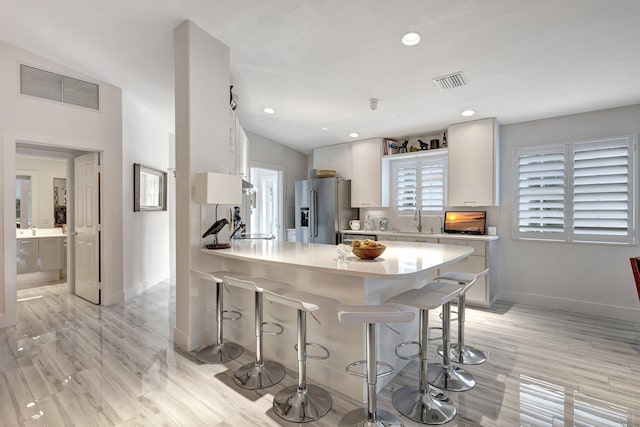 kitchen featuring high quality fridge, sink, white cabinets, a kitchen bar, and kitchen peninsula