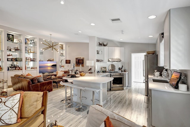 kitchen featuring sink, a breakfast bar area, stainless steel stove, pendant lighting, and white cabinets