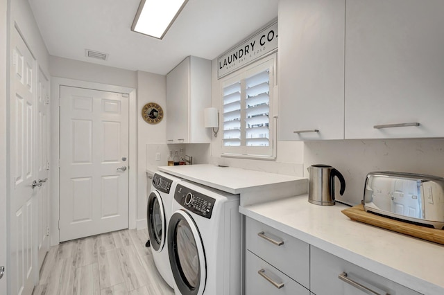 washroom featuring cabinets, washing machine and clothes dryer, and light wood-type flooring