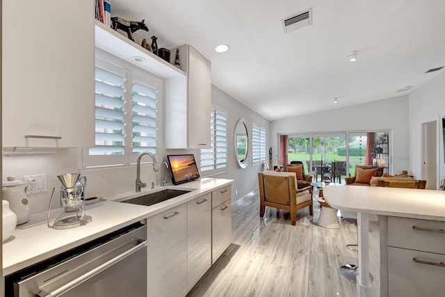 kitchen featuring sink, vaulted ceiling, light hardwood / wood-style flooring, dishwasher, and white cabinets