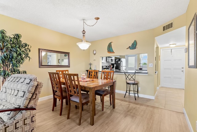 dining area with a textured ceiling and light hardwood / wood-style flooring