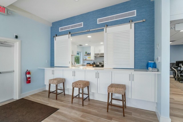 kitchen with a barn door, light hardwood / wood-style floors, kitchen peninsula, a kitchen bar, and white cabinetry