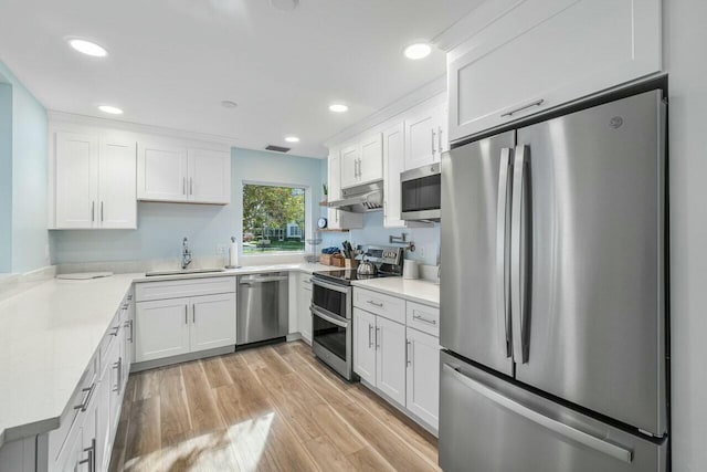 kitchen with appliances with stainless steel finishes, light wood-type flooring, white cabinets, light stone counters, and sink