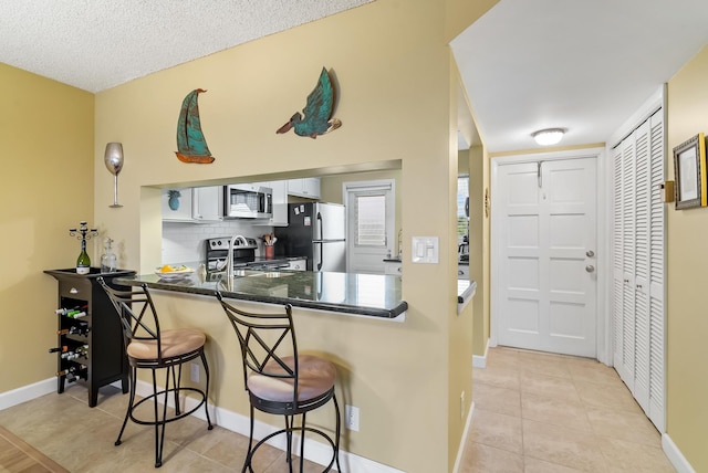 kitchen featuring a kitchen bar, white cabinetry, stainless steel appliances, kitchen peninsula, and light tile patterned floors