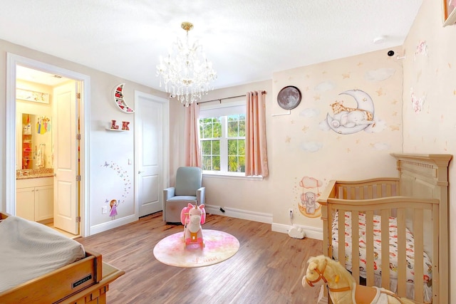 bedroom featuring a crib, a textured ceiling, light hardwood / wood-style flooring, and a chandelier