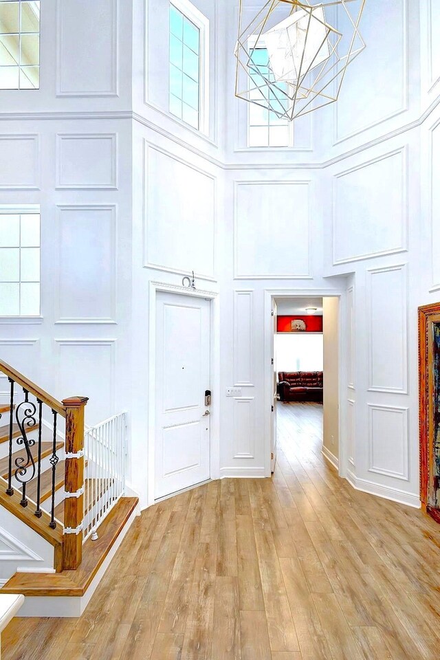 foyer entrance with a towering ceiling, a chandelier, and light wood-type flooring