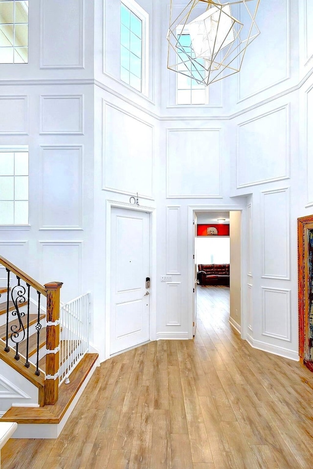 entrance foyer with a notable chandelier, a towering ceiling, and light wood-type flooring