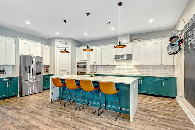 kitchen featuring decorative light fixtures, sink, a kitchen island with sink, stainless steel appliances, and light wood-type flooring