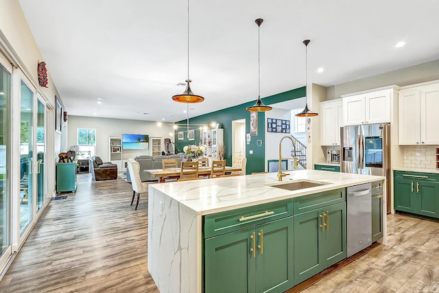 kitchen with decorative light fixtures, an island with sink, white cabinets, green cabinetry, and stainless steel appliances