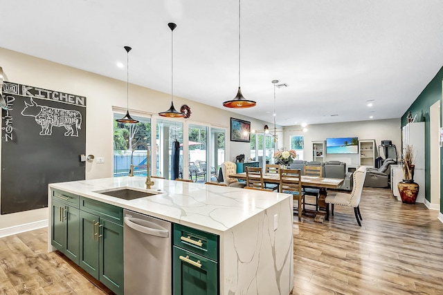 kitchen with sink, light stone counters, green cabinets, an island with sink, and pendant lighting