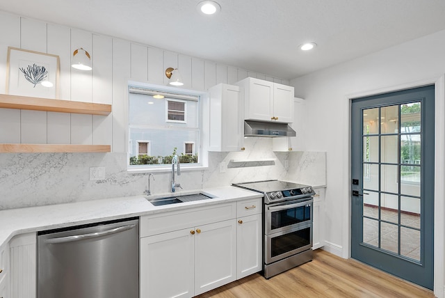 kitchen with light stone countertops, appliances with stainless steel finishes, white cabinetry, light hardwood / wood-style floors, and sink