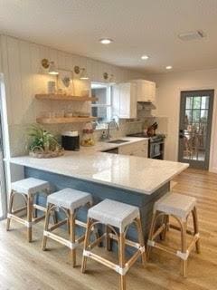 kitchen featuring light hardwood / wood-style flooring, kitchen peninsula, stainless steel electric range oven, and a kitchen bar