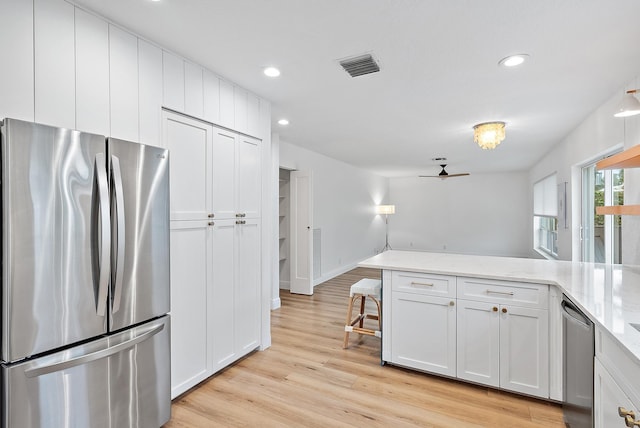 kitchen with light stone countertops, white cabinets, stainless steel appliances, ceiling fan, and light hardwood / wood-style flooring