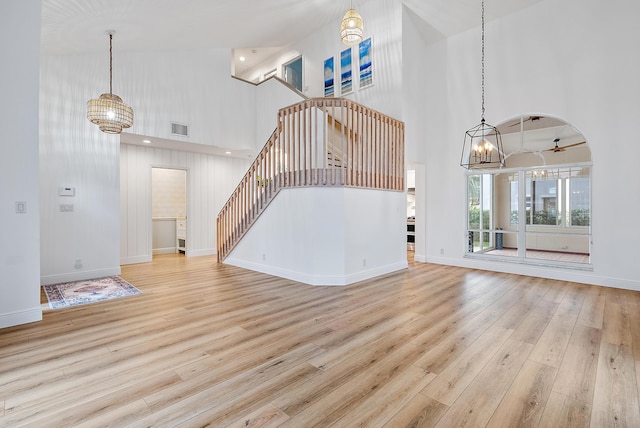 unfurnished living room featuring a notable chandelier, a towering ceiling, and light hardwood / wood-style floors