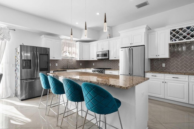 kitchen with stainless steel appliances, white cabinetry, dark stone countertops, and decorative light fixtures