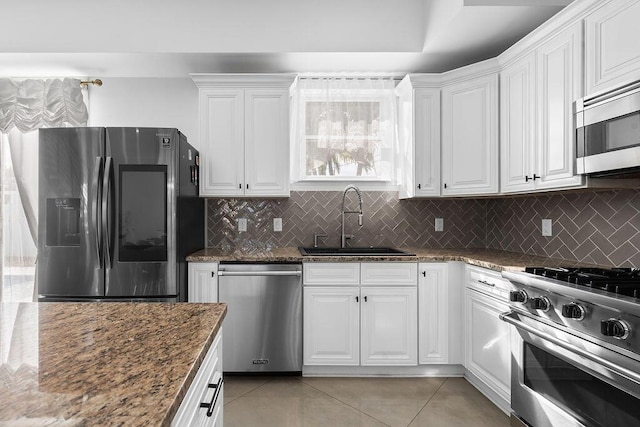 kitchen featuring appliances with stainless steel finishes, white cabinetry, sink, dark stone counters, and light tile patterned floors