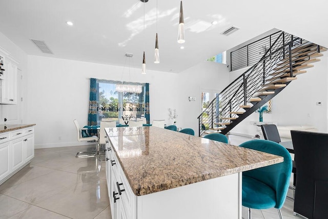 kitchen featuring white cabinetry, decorative light fixtures, light stone countertops, and a center island