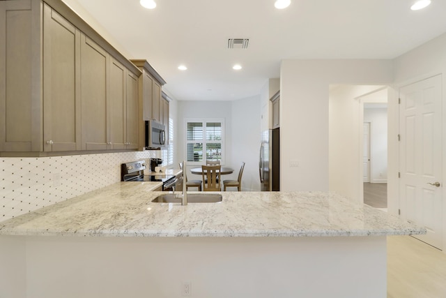 kitchen featuring stainless steel appliances, kitchen peninsula, light stone countertops, and backsplash